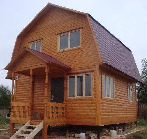 In the photo - a wooden house with a porch on a columnar foundation